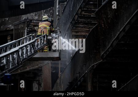 Essen, Deutschland. 21st. Februar 2022. Ein Feuerwehrmann löscht von einer Leiter aus. Im westlichen Viertel der Stadt war seit dem frühen Montagmorgen ein ganzer Wohnblock in Flammen aufgegangen. Das Feuer war kurz nach Mitternacht in der Bargmannstraße ausgebrochen. Die Flammen breiten sich schnell über mehrere Stockwerke aus. Es ist noch unklar, ob Menschen verletzt wurden. Quelle: Fabian Strauch/dpa/Alamy Live News Stockfoto