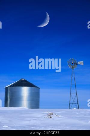 Windmühle und Stahlkornsilos im Winterschnee mit blauem Himmel auf dem Bauernhof für die landwirtschaftliche Landwirtschaft mit Halbmond Stockfoto