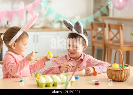 Nettes kleines Mädchen mit ihrem Bruder in Hasen Ohren malen Ostereier zu Hause Stockfoto
