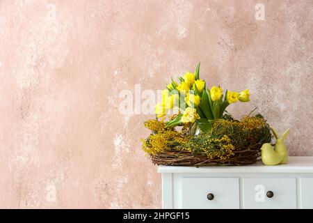 Nest mit schönen Blumen und Ostern Dekor auf dem Tisch neben Farbwand Stockfoto