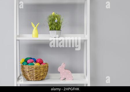 Regal mit Ostereiern und Kaninchen in der Nähe einer hellen Wand im Kinderzimmer Stockfoto