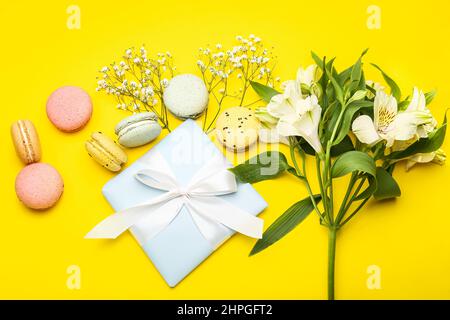 Komposition mit Geschenk zum Internationalen Frauentag, Makronen und Blumen auf gelbem Hintergrund Stockfoto
