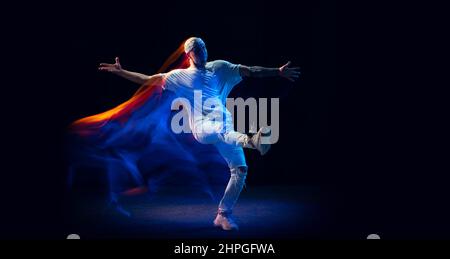 Geteilte Persönlichkeit. Sportlicher Mann in sportlicher weißer Uniform und Do-RAG-tanzendem Hip-Hop isoliert auf dunklem Hintergrund in gemischtem Neonlicht. Jugendkultur Stockfoto