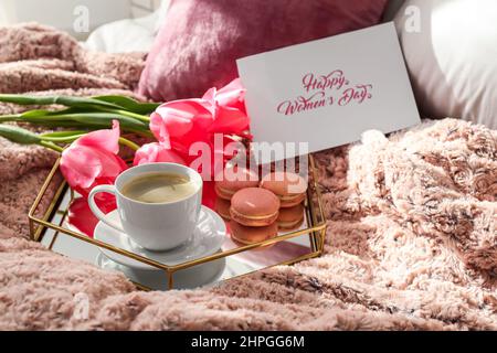 Tablett mit leckerem Frühstück, Grußkarte und Tulpenblumen für die Feier zum Internationalen Frauentag auf dem Bett Stockfoto