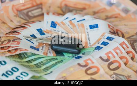 Autoschlüssel auf einem Tisch, der mit 50- und 100-Euro-Banknoten bedeckt ist Stockfoto