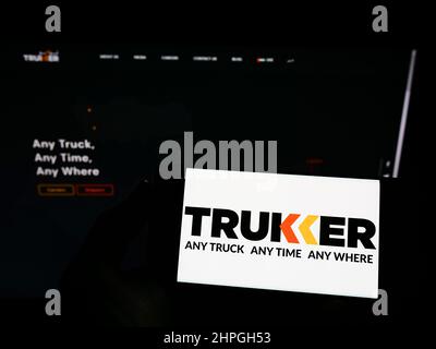 Person, die Smartphone mit Logo des Logistikunternehmens TruKKer Holding Limited auf dem Bildschirm vor der Website hält. Konzentrieren Sie sich auf die Telefonanzeige. Stockfoto