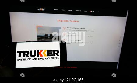 Person, die Mobiltelefon mit Logo des Logistikunternehmens TruKKer Holding Limited auf dem Bildschirm vor der Business-Webseite hält. Konzentrieren Sie sich auf die Telefonanzeige. Stockfoto