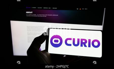 Person, die Mobiltelefon mit dem Logo des amerikanischen NFT-Marktplatzunternehmens Curio Digital Inc. Auf dem Bildschirm vor der Webseite hält. Konzentrieren Sie sich auf die Telefonanzeige. Stockfoto