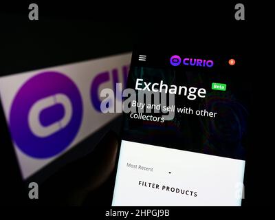 Person mit Mobiltelefon und Webseite des US NFT Marktplatzunternehmens Curio Digital Inc. Auf dem Bildschirm mit Logo. Konzentrieren Sie sich auf die Mitte des Telefondisplays. Stockfoto