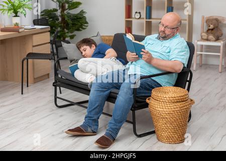 Papa liest ein Buch und Sohn schläft beim Lesen ein. Stockfoto