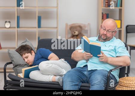 Papa liest ein Buch und Sohn schläft beim Lesen ein. Stockfoto