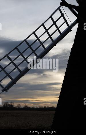 Die silhouettierte Windmühle segelt bei Sonnenuntergang, Wicken Fen National Nature Reserve, Cambridgeshire, England. Stockfoto