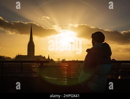 SALISBURY, GROSSBRITANNIEN. Ein Mann beobachtet den Sonnenuntergang über der Kathedrale von Salisbury bei viel ruhigeren Bedingungen nach Tagen starker Winde und heftiger Regenfälle in Wiltshire, Großbritannien. Datum: 21/02/2022. Kredit: Matthew Lofthouse/Alamy Live Nachrichten Stockfoto