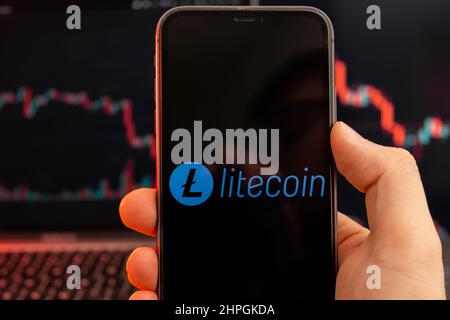 Litecoin LTC-App zur Analyse der Kryptowährung-Aktienmärkte auf dem Bildschirm von Mobiltelefonen in Menschenhand und Abwärtstrenddiagrammen, Handelsdaten im Hintergrund, Februar 2022, San Francisco, USA. Stockfoto