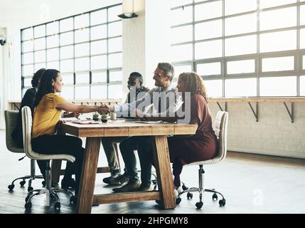 Herzlichen Glückwunsch - Sie haben es verdient. Aufnahme von zwei Geschäftskollegen, die während eines Meetings die Hände über den Sitzungstisch schüttelten. Stockfoto