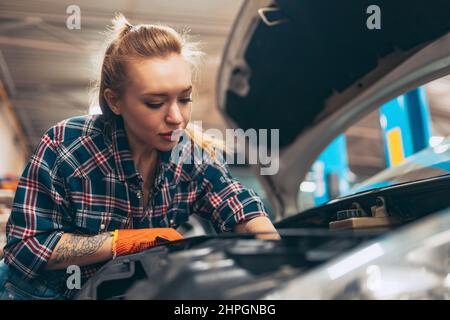 Autoabfahren. Junge rothaarige Mädchen, Auto-Mechaniker arbeiten an der Auto-Service-Station mit verschiedenen Arbeitswerkzeugen. Gleichstellung der Geschlechter. Arbeit, Beruf, Auto Stockfoto