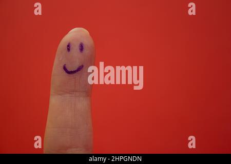 Smiley-Gesicht auf Finger isoliert auf rotem Hintergrund gezeichnet. Glücklichsein und lächelndes Konzept. Stockfoto