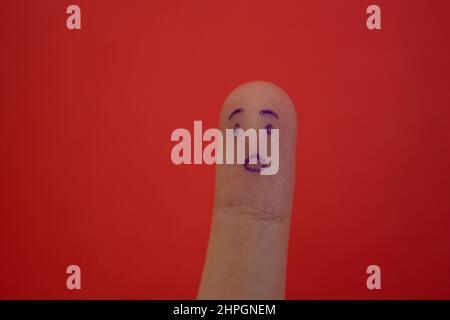 Schockiertes Gesicht auf Finger isoliert auf rotem Hintergrund gezeichnet. Witziger Gesichtsausdruck am Finger. Stockfoto