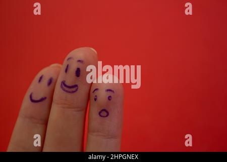 Lächelnde und schockierte Gesichter, die auf den Fingern auf rotem Hintergrund isoliert dargestellt werden. Lustige Gesichtsausdrücke an den Fingern. Stockfoto