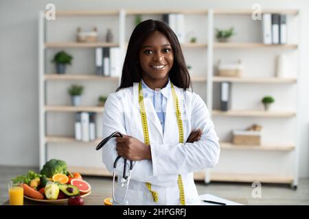 Porträt eines freundlichen afroamerikanischen Ernährungswissenschaftlerin mit Maßband und Stethoskop, das eine gesunde Ernährung empfiehlt Stockfoto