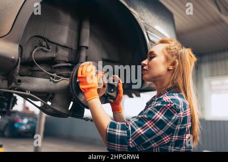 Autoabfahren. Junge rothaarige Mädchen, Auto-Mechaniker arbeiten an der Auto-Service-Station mit verschiedenen Arbeitswerkzeugen. Gleichstellung der Geschlechter. Arbeit, Beruf, Auto Stockfoto