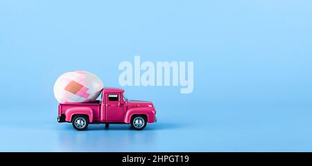 Rosafarbenes Auto auf blauem Hintergrund mit einem Osterei im Rücken. Stockfoto
