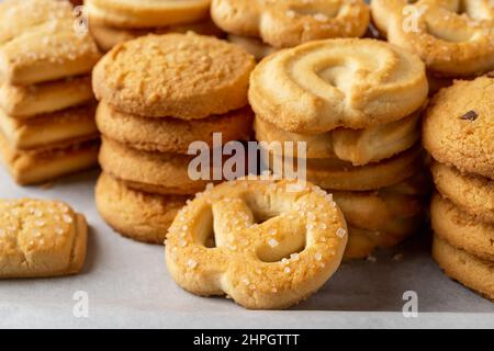 Zuckerbrezel gegen gestapelte Shortbread-Kekse auf einem weißen Backpapier. Verschiedene knusprige Butterkekse aus nächster Nähe. Leckeres danis-Gebäck. Makro. Stockfoto