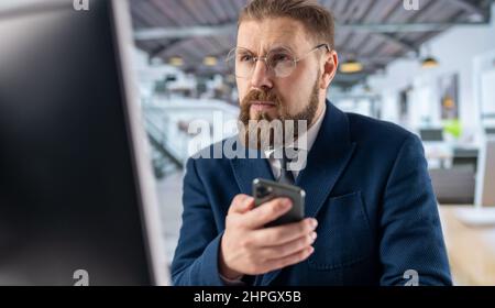 Mann, der im Büro Mobil und pc benutzt Stockfoto