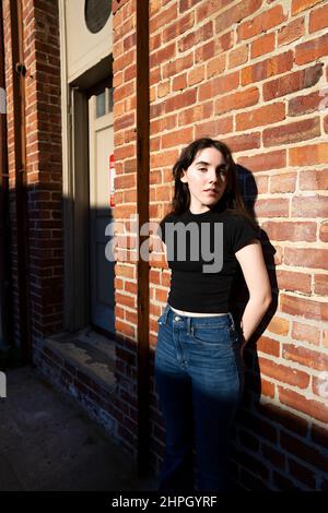 Junge Frau in Retro-Kleidung, die vor einer Ziegelwand steht Stockfoto