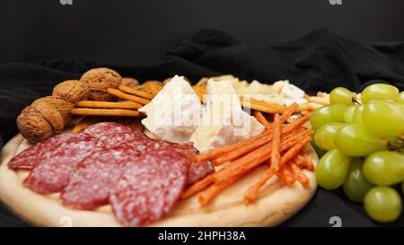 Käseplatte mit verschiedenen Käsesorten, Trauben, Nüssen auf schwarzem Hintergrund. Italienische Käseplatte für Wein. Stockfoto