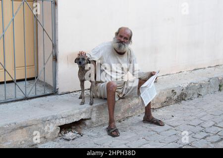 Mann mit Zeitung reibt den Kopf seines Haustierhundes auf einer Straße in Havanna, Kuba. Stockfoto