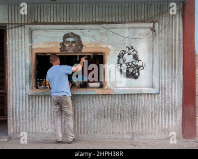 Mann in einem Geschäft, der Waren kauft, mit einem Wandbild des kubanischen Helden Che Guevara auf der Fensterbank. Stockfoto