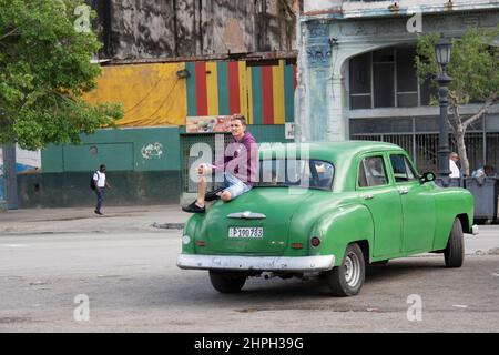 Junger Mann, der auf dem Kofferraum eines alten amerikanischen Autos in Havanna, Kuba, sitzt. Stockfoto