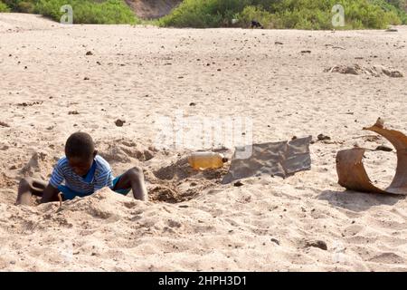 In Binga wird ein kleiner Junge im Sand eines ausgetrockneten Flusses nach Wasser gegraben. Trotz seiner Nähe zum Zambezi-Fluss, erlebt Binga andauernde Wasserknappheit und viele Flüsse trocknen aus. Simbabwe. Stockfoto