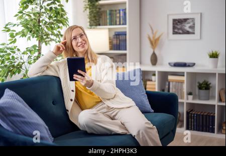 Verträumte Frau auf dem Sofa mit Tablet Stockfoto