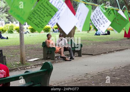 Ein Paar wird durch eine Gebetslinie gesehen, die auf einer Parkbank auf dem Africa Unity Square in Harare, Simbabwe, sitzt. Stockfoto