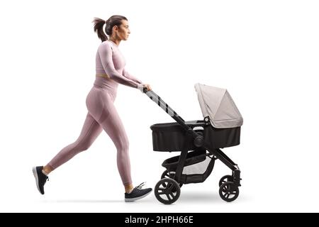 Ganzprofil-Aufnahme einer Mutter in Crop Top und Leggings, die mit einem Kinderwagen auf weißem Hintergrund isoliert läuft Stockfoto