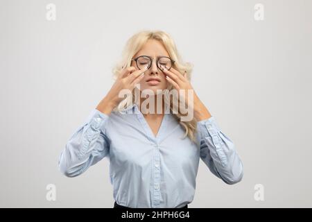 Müder Büroangestellter, der die Augen berührt, eine Brille trägt und unter einer Belastung der Augen leidet und Probleme mit dem Sehvermögen hat Stockfoto