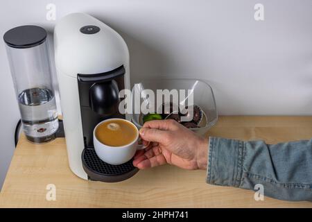 Nahaufnahme der männlichen Hände, die einen Becher gegossenen Kaffees aus der Kapselkaffeemaschine nehmen. Schweden. Stockfoto