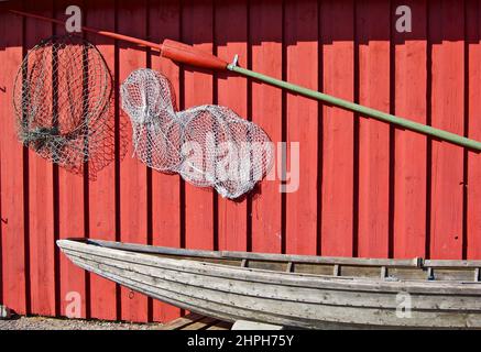 Angelausrüstung hängt an der roten Gebäudewand hinter einem alten Holzboot. Stockfoto