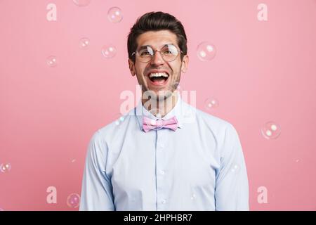 Junger weißer Mann mit Fliege, lachend und isoliert auf rosa Hintergrund auf die Kamera schauend Stockfoto