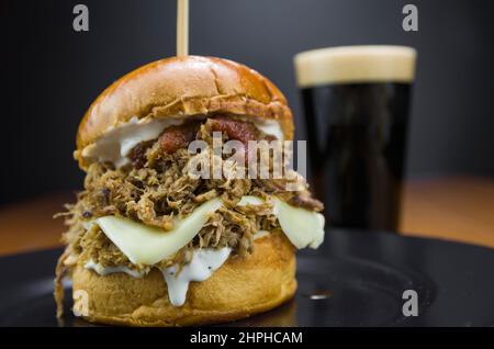 Nahaufnahme von leckeren hausgemachten Schweineburger auf Holztisch und schwarzem Hintergrund Stockfoto
