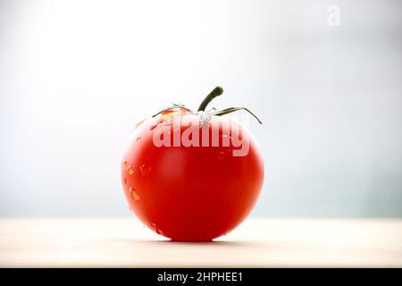 Frisch gereifte rote Tomate auf Schneidebrett. Seitenansicht mit hellem, bullroten Hintergrund. Stockfoto