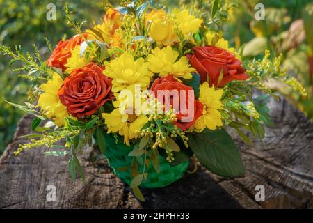 Bouquet of Flowers ist eine Komposition aus roten Rosen und Chrysanthemen, die auf einem Holzstumpf auf einem grünen Grasgrund liegen. Der Hintergrund für die Postca Stockfoto