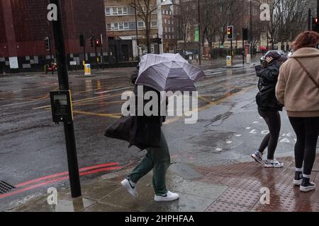 Frau, die während des stürmischen Wetters in London, Großbritannien, mit ihrem Regenschirm kämpft Stockfoto