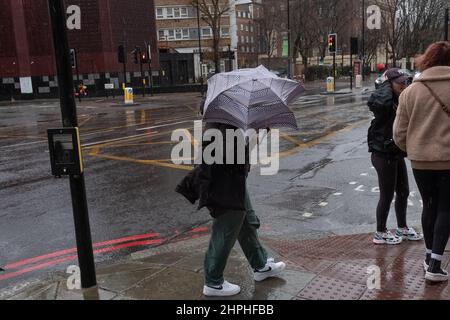 Frau, die während des stürmischen Wetters in London, Großbritannien, mit ihrem Regenschirm kämpft Stockfoto