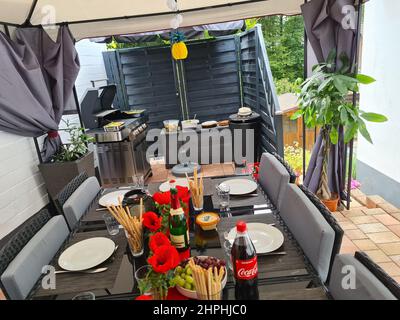 HEILIGENHAUS, NRW, DEUTSCHLAND - 30. JUNI 2020: Auf der Terrasse Spaß haben, Bier trinken und plaudern, während ihre Freunde das auf der Terrasse gebratene Fleisch servieren Stockfoto