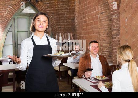 Positive Kellnerin, die den Besuchern das Restaurant vorführte Stockfoto