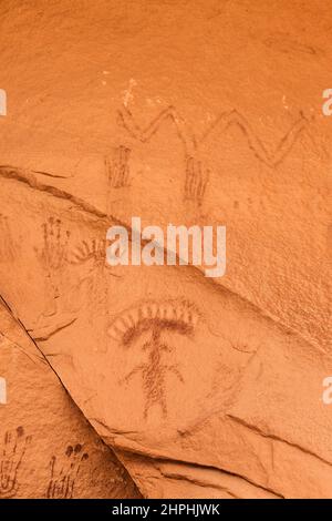 Eine uralte gemalte Felsenkunst oder Piktogramm-Tafel mit anthropomorphen Figuren, die fantastische Kopfbedeckungen tragen. Befindet sich unter einem geschützten Stockfoto