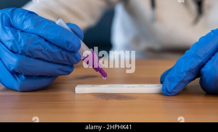 Ein Mann mit Latexhandschuhen, der die Probe in das covid-19-Antigendiagnosetestgerät legt. Set mit Kassettenkit für Selbsttests zum Einchecken Stockfoto